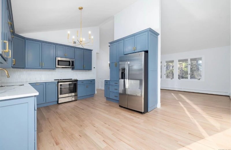 The same kitchen after remodeling with blue cabinets, hardwood floor, and updated finishes by Cross Tiles